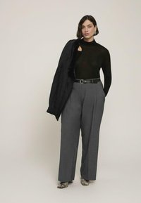 Czarny przezroczysty golf, szare spodnie z wysokim stanem z zakładkami, czarny pasek i czarna kurtka zarzucona na ramię. Buty w wężowy wzór.