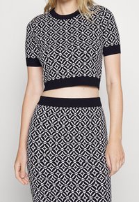Czarny i biały dzianinowy top z krótkimi rękawami o kroju cropped oraz geometrycznym wzorze; pasuje do spódnicy o podobnym wzorze.