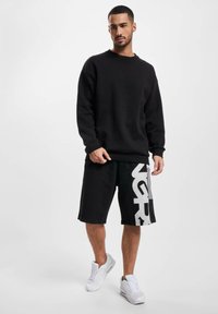 Black sweatshirt with a round neck, paired with black shorts featuring a white logo. White sneakers complete the outfit.