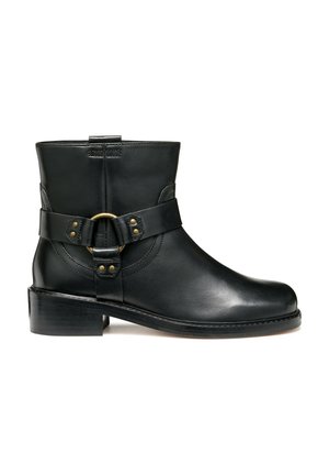 Bottine en cuir noir à bout arrondi, avec une sangle latérale ornée d'une boucle dorée circulaire et un talon bas empilé. Texture lisse et détails minimalistes.