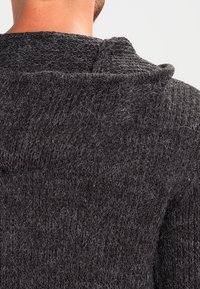 Ciemnoszara, teksturowana bluza z kapturem o luźnym kroju, z regulowanym kapturem i wyraźnie miękkim materiałem z widocznymi włóknami.