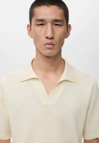 Camiseta polo de manga corta en color amarillo claro, confeccionada con tejido de punto texturizado que presenta un escote en V y cuello plano.