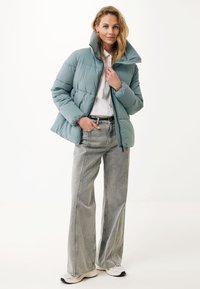 Padded light blue jacket with a high collar, paired with gray wide-leg jeans and white sneakers. The jacket features a zipper closure and stitched panels.