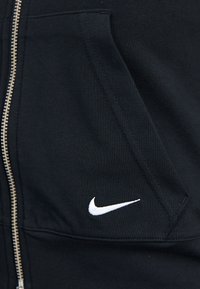 Sweatshirt preto com fecho éclair, feito de uma mistura de algodão, apresentando bolsos cosidos, um logótipo branco da Nike e um tecido texturado com rib ribbing subtil.