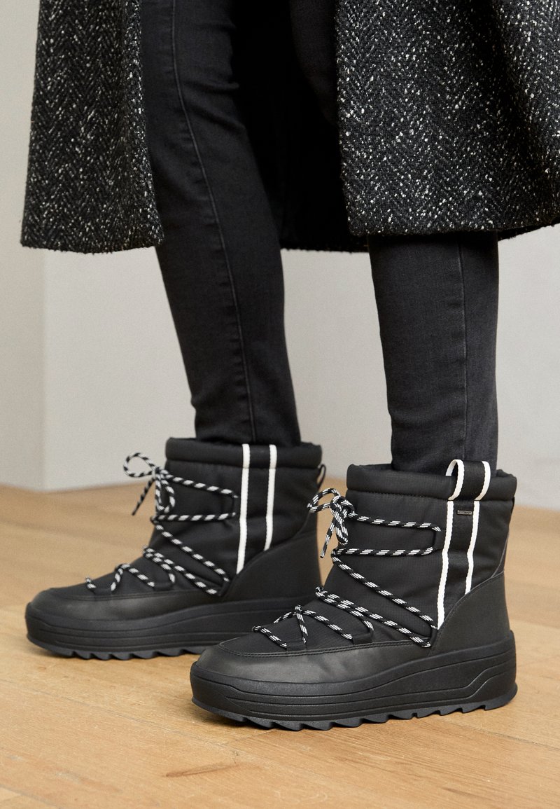 Czarne wodoodporne buty z wyściełanym cholewką, białymi paskami i sznurowadłami w czarno-białej tonacji. Teksturowana gumowa podeszwa zapewniająca przyczepność i stabilność.
