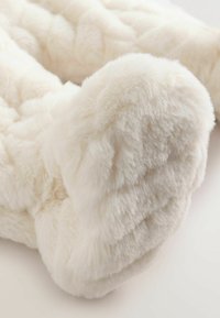 Cremefarbener Kunstfellwurf mit geflochtenem Textur und weicher, flauschiger Oberfläche. Abgerundete Kanten betonen das plüschige Material und die Designdetails.