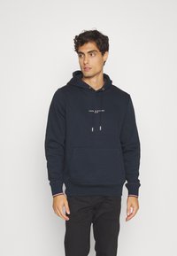 Felpa blu navy in misto cotone con cappuccio regolabile e tasca frontale. Presenta un logo bianco sulla parte anteriore e polsini a costine.