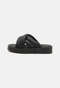 Sorte skridsikre sandaler med en polstret sål, som har krydsede læderstropper og en tykk platformssål. Glat tekstur og minimalistisk design.