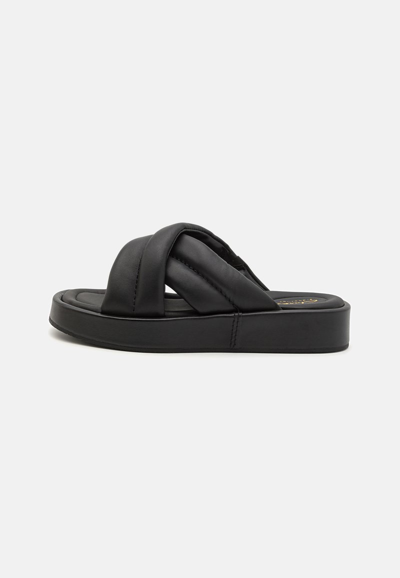 Sandal com plataforma preta, possui uma base acolchoada, apresentando tiras de couro cruzadas e um solado espesso. Textura suave e design minimalista.