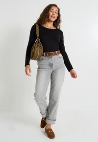 Haut noir à manches longues, jean taille haute gris, mocassins en daim marron et sac à main vert olive. Design simple avec des poignets roulés et une bandoulière tressée.