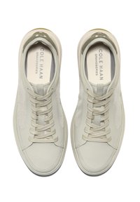 Světlé šedé tenisky s texturovaným koženým a síťovaným svrškem, kulatou špičkou, šněrovacím designem a minimalistickým profilem. Název značky viditelný na stélkách.