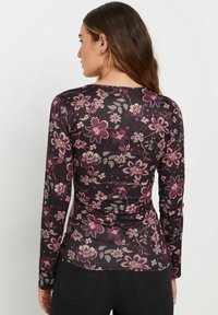 Pitkähihainen t-paita tumman violetissa sävyssä, jossa on vaaleanpunaisia ja kermankeltaisia kukkakuoseja. Hyvin istuva malli, jossa on pyöreä kaula-aukko ja sileä rakenne.