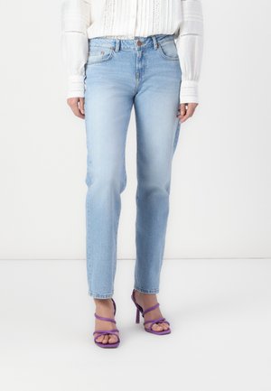Jean en denim bleu clair avec une coupe droite, design à cinq poches et décoloration subtile, associés à des sandales à talons hauts strappées violettes.