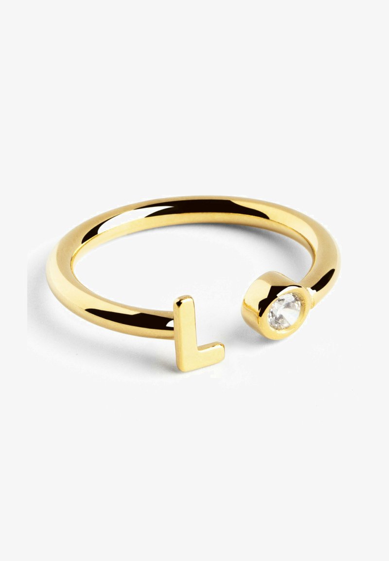 Bague dorée à l'aspect minimaliste, ornée d'un accent en "L" d'un côté et d'une pierre précieuse transparente sertie dans un monture ronde de l'autre côté.