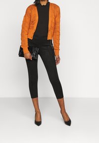 Orangefärgad, strukturerad stickad kofta med knappar, kombinerad med svarta leggings och en svart clutch. Högklackade skor kompletterar outfiten.
