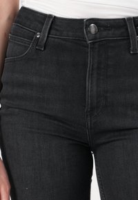 Høytlivde svarte denim jeans med en glatt tekstur, to frontlommer, en metallknapp og rene sømdetaljer.
