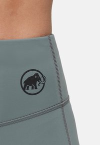 Leggings de sport gris avec des coutures contrastées et un logo mammouth noir bien visible sur la hanche. Texture lisse, design ajusté.