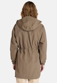 Veste marron à capuche avec taille et poignets élastiqués, dotée d'un matériau lisse et léger ainsi que d'une silhouette droite.