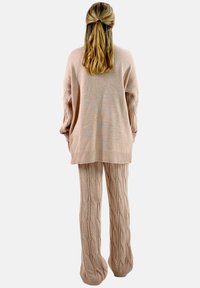 Trui- en broekset in zacht beige gebreide stof. De trui heeft een losse pasvorm en een geribbelde zoom. De broek heeft een getextureerd kabelgebreid patroon.