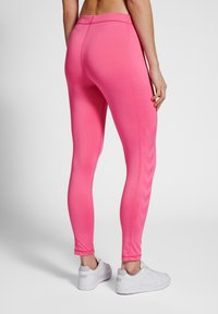 Leggings ajustés à taille haute en tissu rose vif. Dotés d'un motif en chevrons sur le côté. Associés à des chaussures de sport blanches.