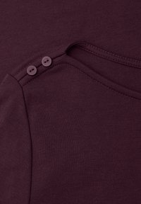 Detailní záběr tmavě fialové tkaniny se dvěma ladícími knoflíky na švové linii ramene oděvu.