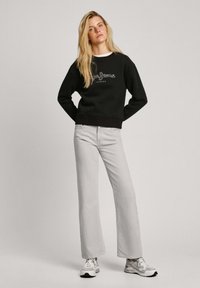 Sudadera negra con logo bordado, combinada con jeans rectos de tiro alto en gris claro y zapatillas blancas. Diseño sencillo, corte relajado.