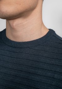 Ciemnoniebieski sweter prążkowany z okrągłym dekoltem, z teksturowaną powierzchnią i subtelnymi różnicami w wzorze tkaniny.