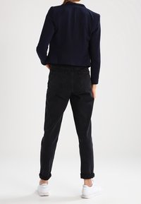 Marinblå kort jacka med strukturerade axlar, kombinerad med svarta högmidjade jeans och vita sneakers. Enkelt, rent design utan utsmyckningar.