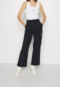 Svarta byxor med vida ben, i en slät textur och framfickor, kombinerat med en figurnära vit linne med en liten logotyp.