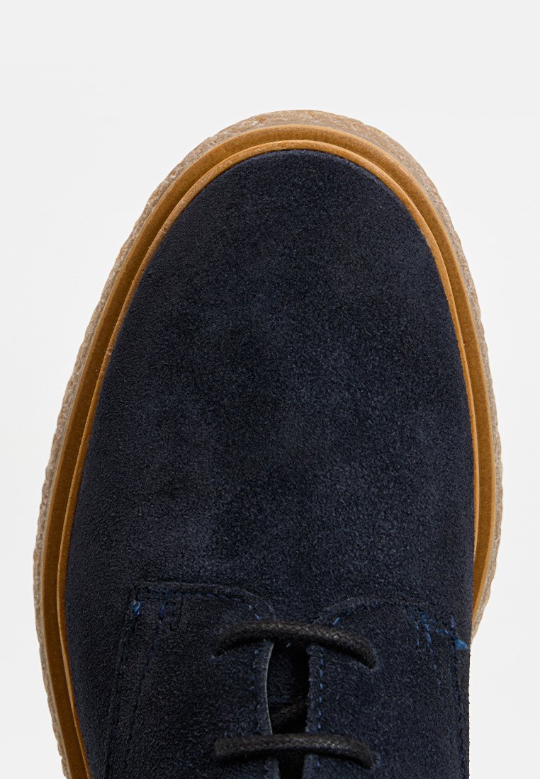 Marineblaues Wildlederschuhwerk mit runder Zehe, flacher brauner Sohle und schwarzen Schnürsenkeln. Sichtbare Nähte und eine strukturierte Oberfläche verleihen dem Design Charakter.