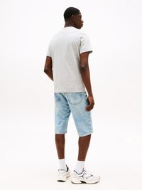 Graues Baumwoll-T-Shirt, lässiger Schnitt, kombiniert mit hellblauen Denim-Shorts. Getragen mit weißen Socken und Sneakers, was einen lässigen Stil zeigt.