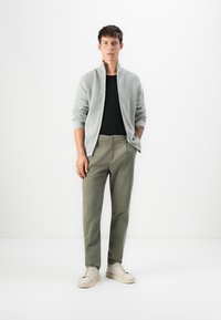 Lys grå ribbestrikket zip-genser over en sort skjorte, kombinert med olivengrønne chinos og off-white sneakers. Enkelt design, uformell stil.