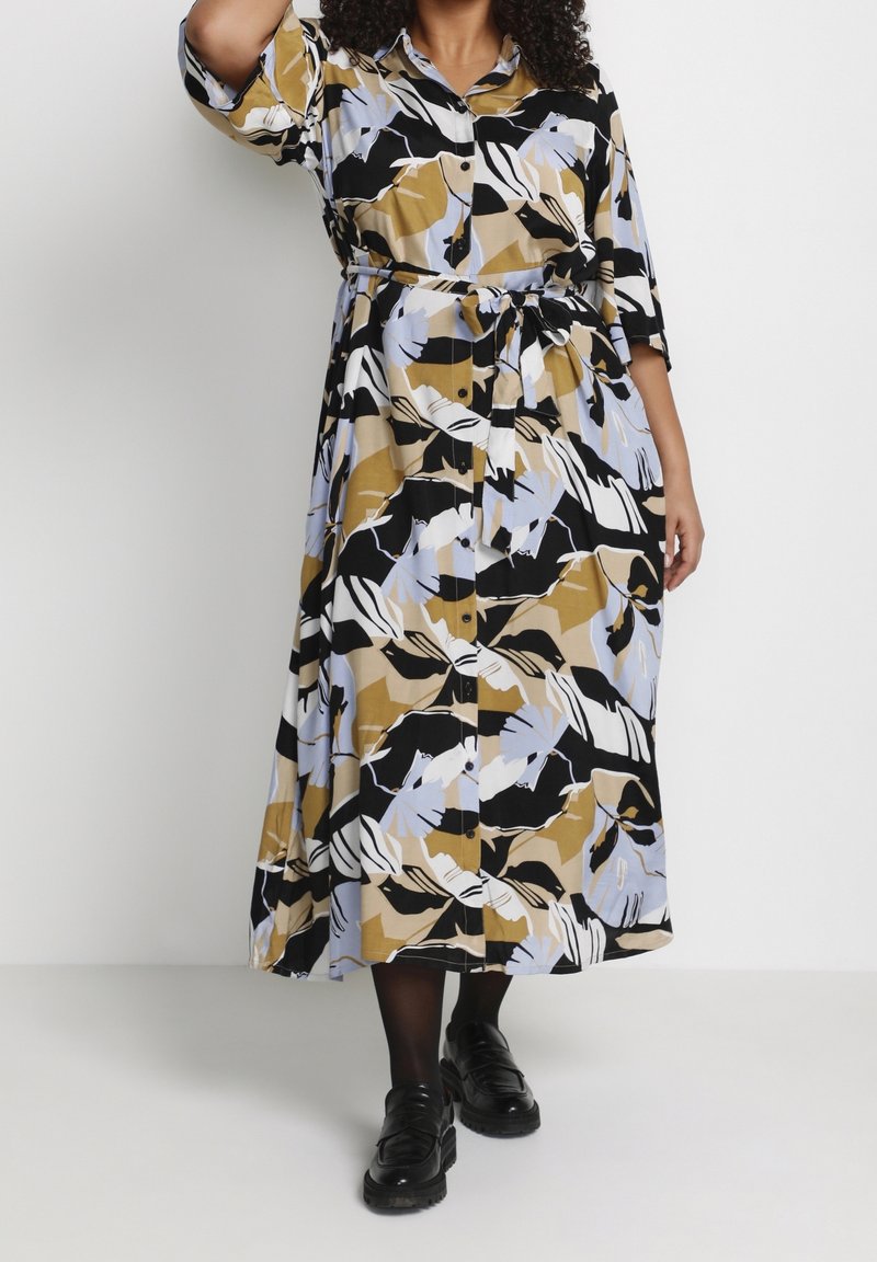 Robe longue en tissu à motifs avec des couleurs noir, beige et bleu clair. Modèle boutonné avec une ceinture à la taille et des manches courtes.