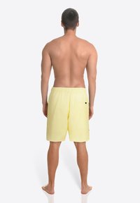 Gelbe Badehose mit elastischem Bund und einer einzelnen Gesäßtasche, aus leichtem Stoff, von hinten gezeigt.