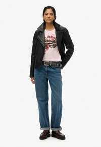 Chaqueta de cuero negra de motorista sobre una camiseta gráfica rosa, combinada con jeans de mezclilla azul claro y zapatos de plataforma negros. Cinturón negro con tachuelas.