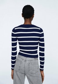Maglietta a righe navy e bianca a maniche lunghe con scollo rotondo, abbinata a jeans grigi a vita alta.