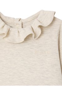 Helles Beige, weicher Baumwolloberteil mit Volant-Ausschnitt und gesticktem Markennamen in passender Farbe. Schlichte und strukturierte Stoffoberfläche.