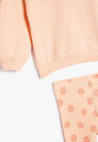 Sudadera de algodón melocotón con puños acanalados, combinada con leggins acanalados melocotón que presentan patrones de flores naranjas. Diseño de corte relajado.