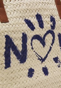 Kudottu olkilaukku, jossa on ruskea nahkahihna ja sinisellä maalatut abstraktit kukka- ja sydämenmuotoiset kuviot luonnonvärisellä kuitupinnalla.