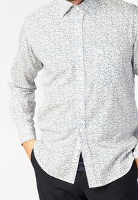 Biała koszula z guzikami z niebieskim kwiatowym wzorem. Długie rękawy i klasyczny kołnierzyk. Materiał wydaje się lekki i gładki w dotyku.