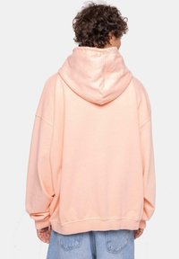 Sudadera extragrande en tela de melocotón claro, con una gran capucha, hombros caídos y dobladillo acanalado. Algodón texturizado con un corte relajado.