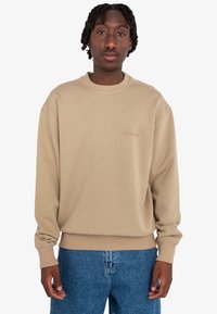 Sudadera beige con cuello redondo, puños y dobladillo acanalados, y un sutil logo bordado de "Element" en la parte delantera. Combinada con jeans azules.