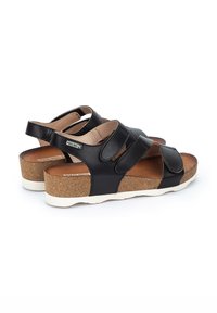 Sandalias de cuero negro con plantilla de corcho, correas ajustables y suela de goma blanca. Presentan una forma redondeada y textura suave.