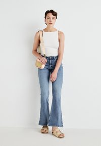 Hvid tænk top, lyseblå flared jeans, beige sandaler og en lille crossbody taske med en orange rem og gule accenter.