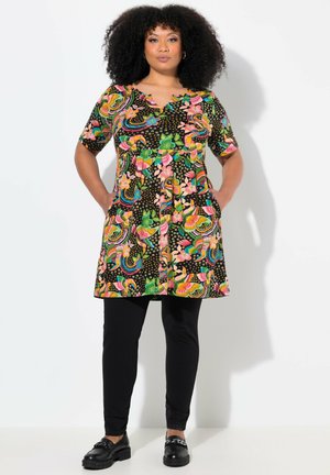Robe colorée avec un motif floral et arc-en-ciel sur fond noir, à manches courtes, décolleté en V et poches latérales, associée à des leggings noirs.