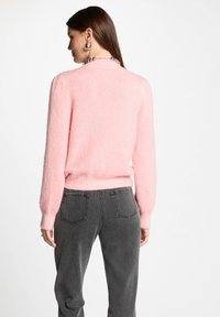 Zacht roze, pluizig sweater met een ronde halslijn, lange mouwen en geribbelde manchetten, gecombineerd met donkergrijze denim jeans met achterzakken.