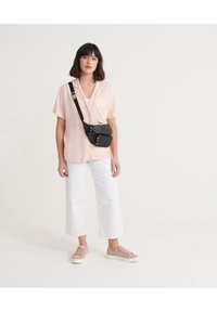 Camicia rosa chiaro a maniche corte con righe verticali, pantaloni bianchi a gamba larga, borsa a tracolla nera e sneakers rosa chiaro.