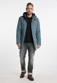 Giacca parka isolata blu con cappuccio, caratterizzata da una zip frontale, due tasche laterali e un logo sul petto. Indossata sopra una maglietta nera.