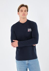 Marineblaues Langarmshirt mit Rundhalsausschnitt, das den weißen Schriftzug "Athletic 1968" und einen gestreiften Akzent aufweist. Hergestellt aus glattem, weichem Material.
