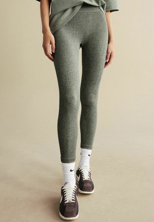 Leggings verzi cu textură ribbată, cu un design ajustat, purtate cu șosete albe Nike și pantofi atletici maro.